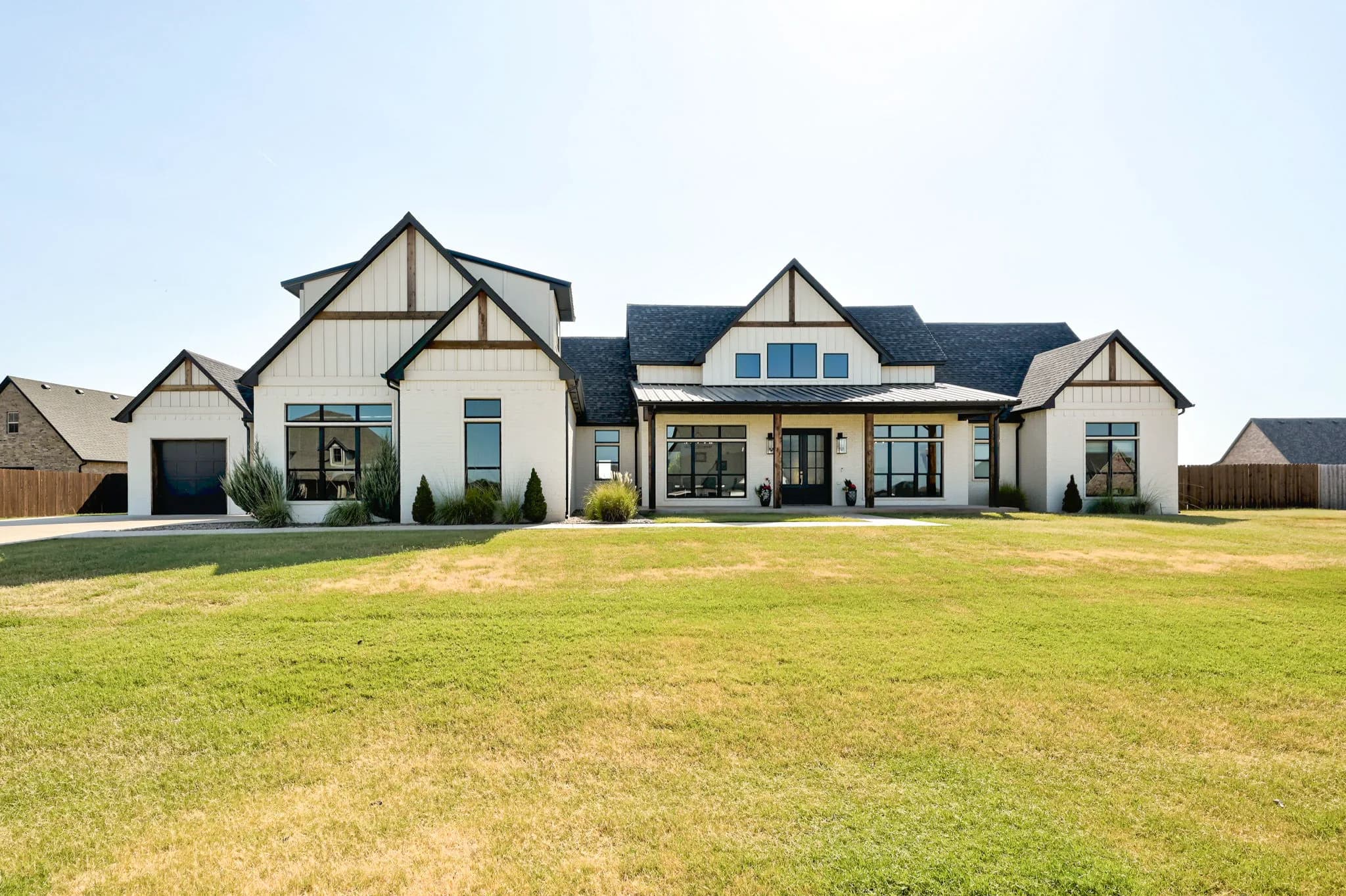 Front exterior of the white-brick modern farmhouse at 1034 Acclivis Way, with a covered porch, black metal roof accents, and a manicured lawn
