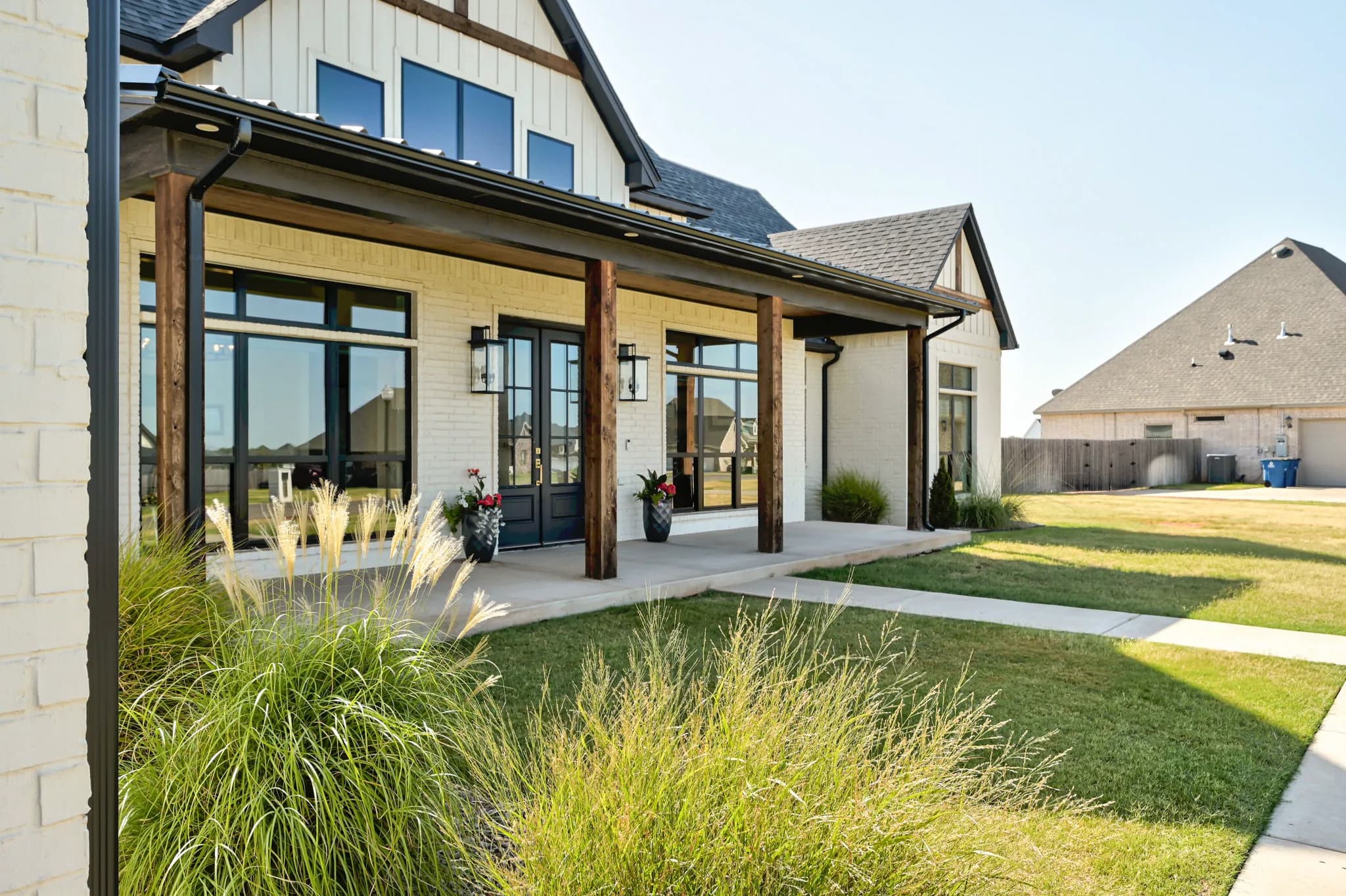Covered front porch with stained cedar posts and native-grass landscaping beside the walkway
