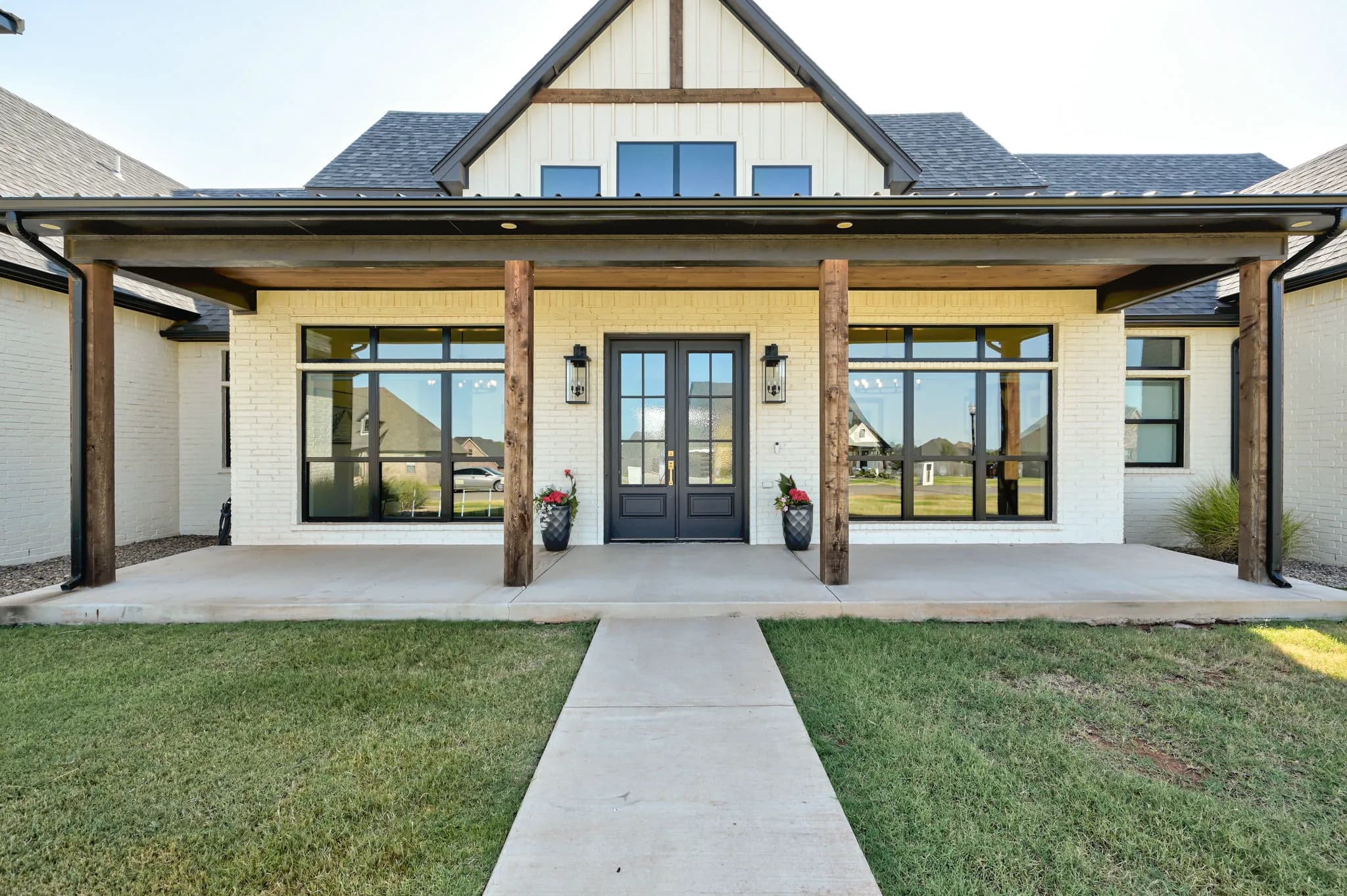 Symmetrical covered entry porch with black double doors framed by cedar columns and picture windows