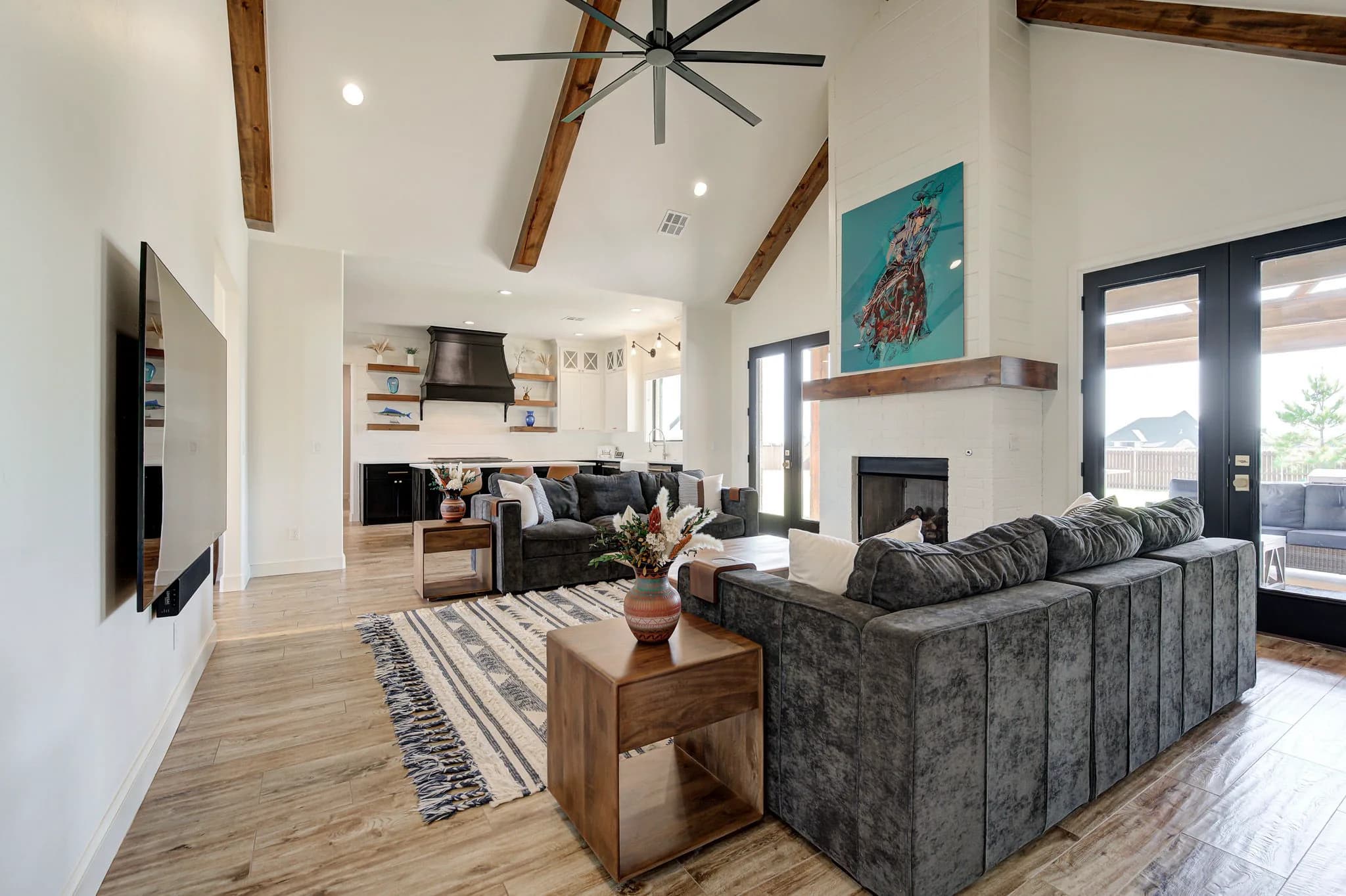 Open-concept living room with a mounted TV and vaulted beamed ceiling, open to the kitchen