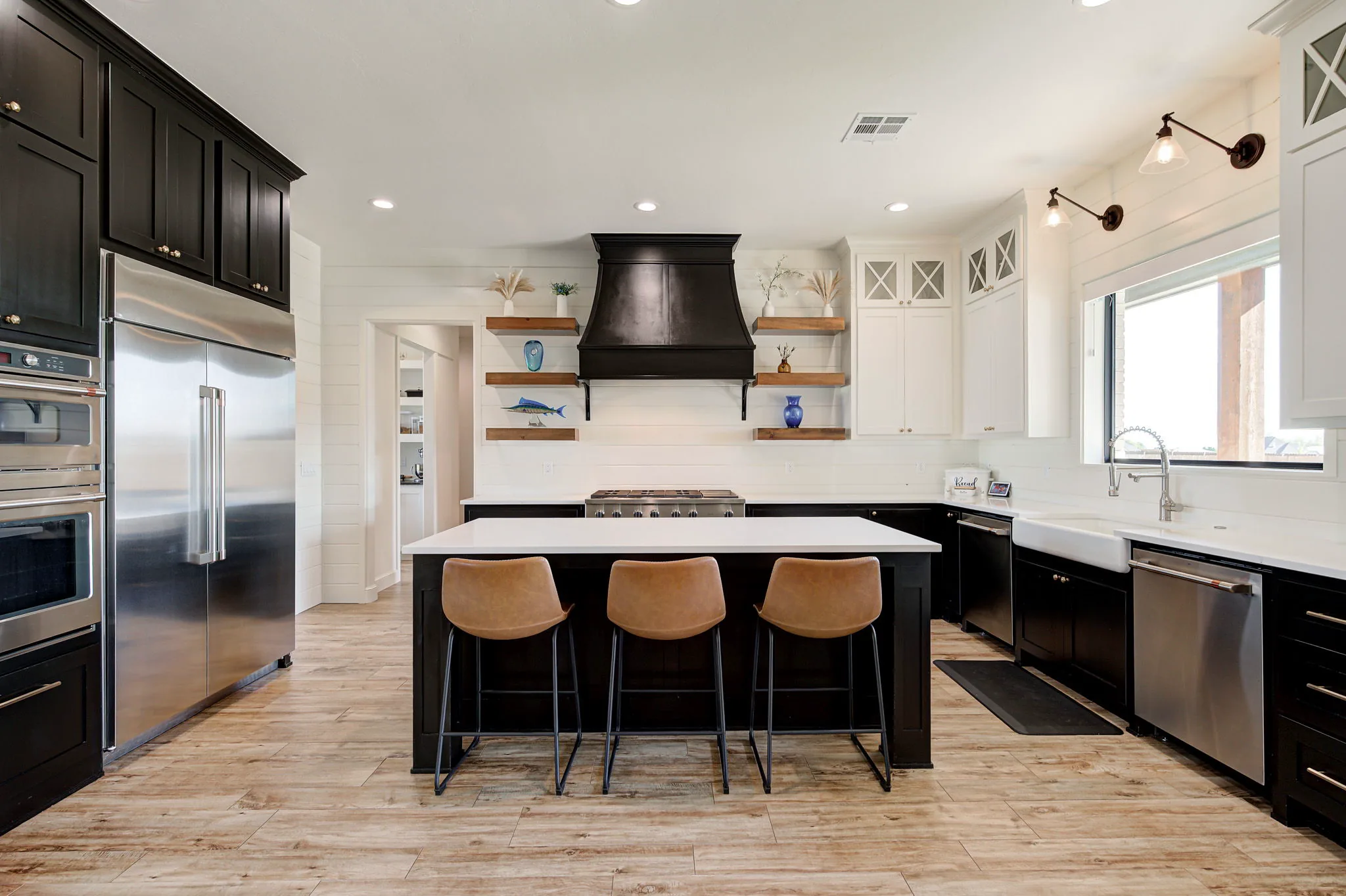 Kitchen with a black range hood, waterfall-edge island, gas cooktop, and leather bar stools