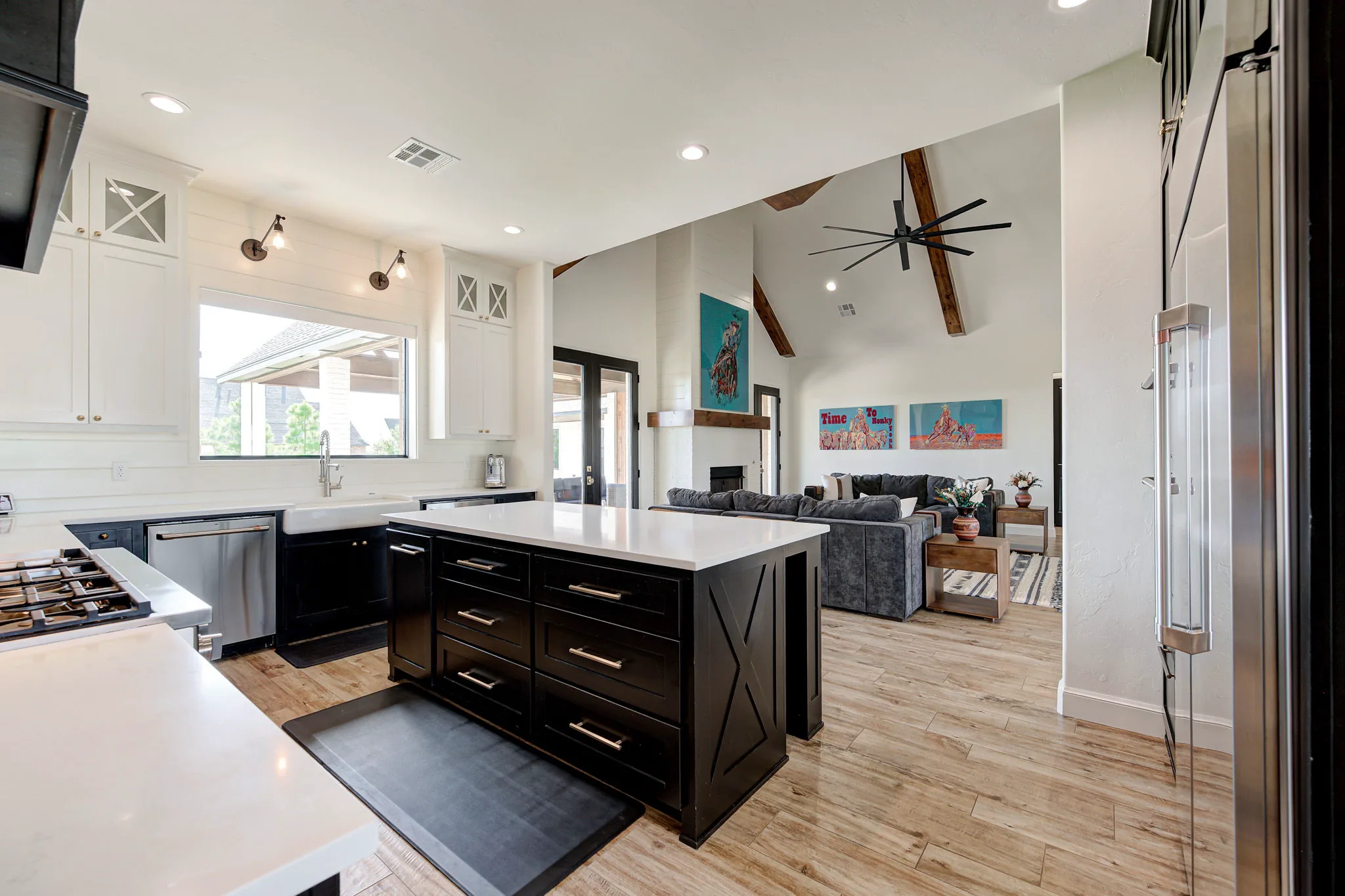 Kitchen open to the great room, with a black waterfall-edge island, a farmhouse sink, and a stainless refrigerator beneath a vaulted beamed ceiling