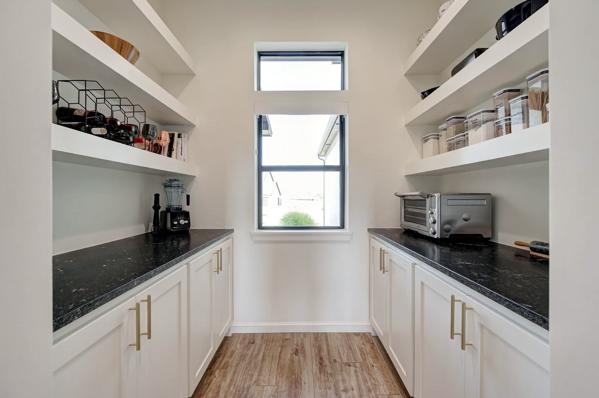 Butler's pantry with white cabinetry, black leathered-granite counters, and floating shelves for storage
