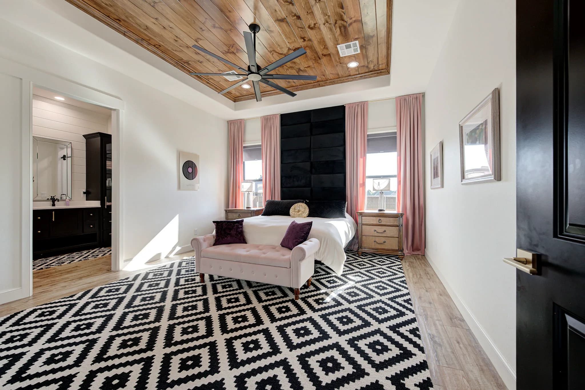 Primary bedroom with a knotty-pine tray ceiling, an upholstered accent wall, and an adjoining ensuite bath