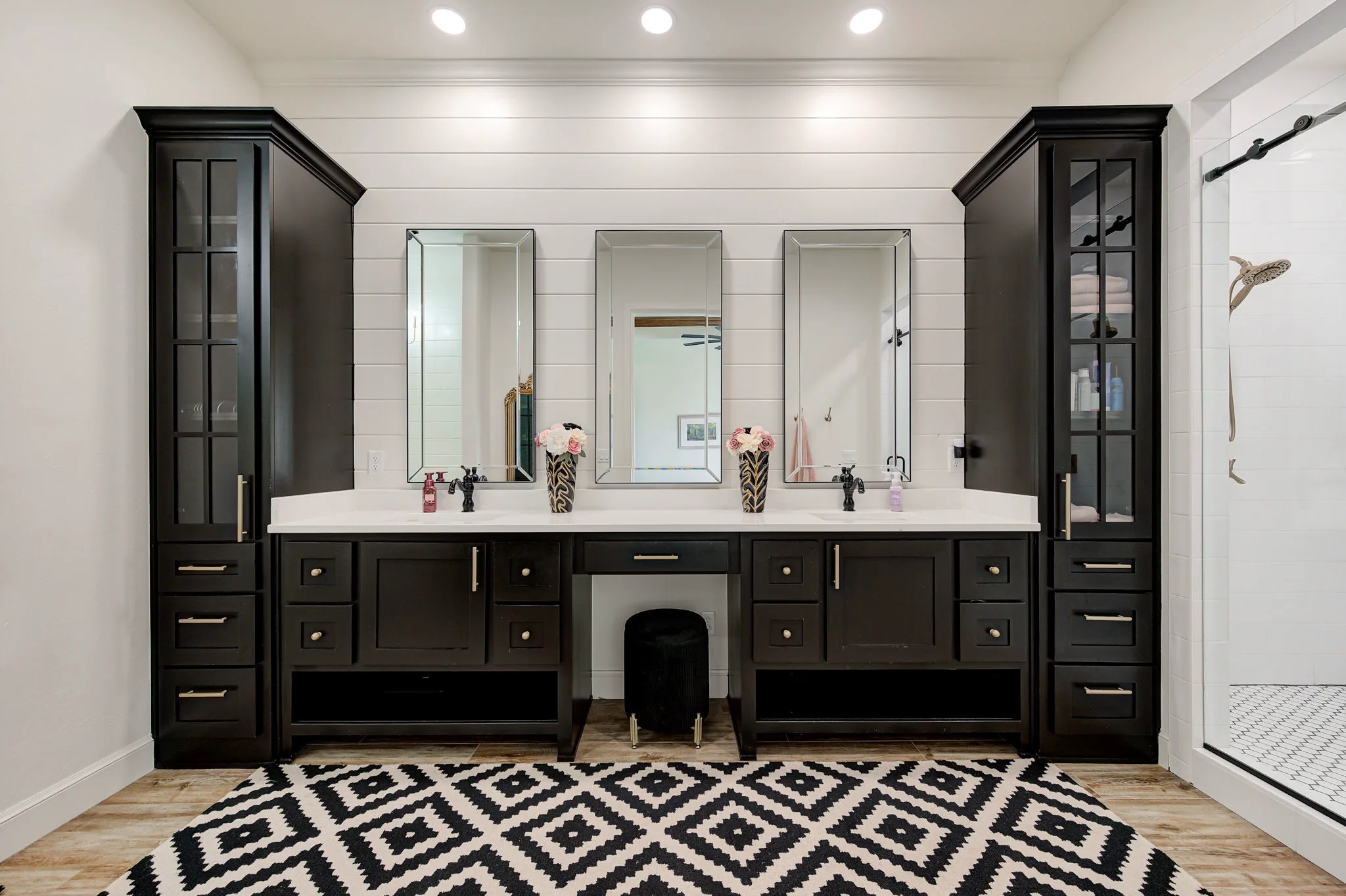 Primary ensuite with a double vanity, framed mirrors, a seated makeup station, and a glass walk-in shower