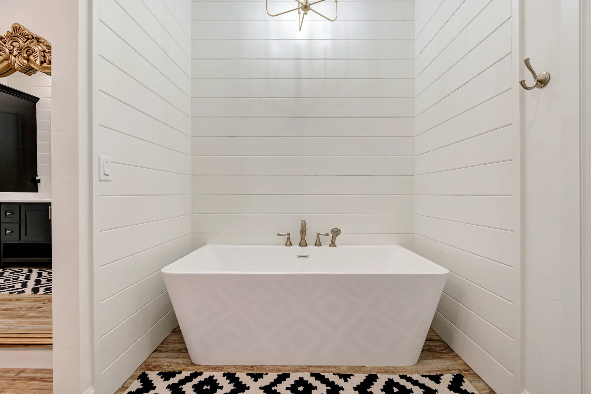 Freestanding soaking tub set in a shiplap alcove with a brushed-gold tub filler