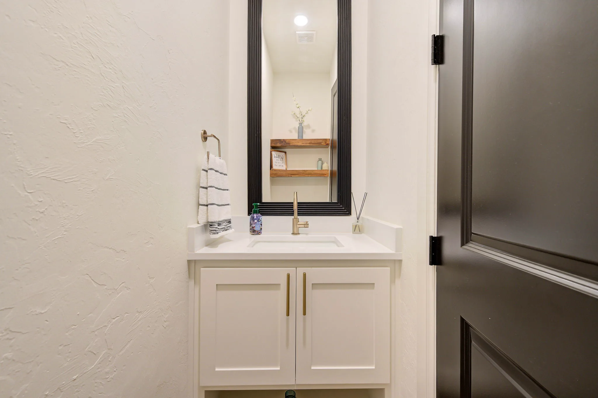 Powder room with a white vanity, a black-framed mirror, and rustic floating shelves