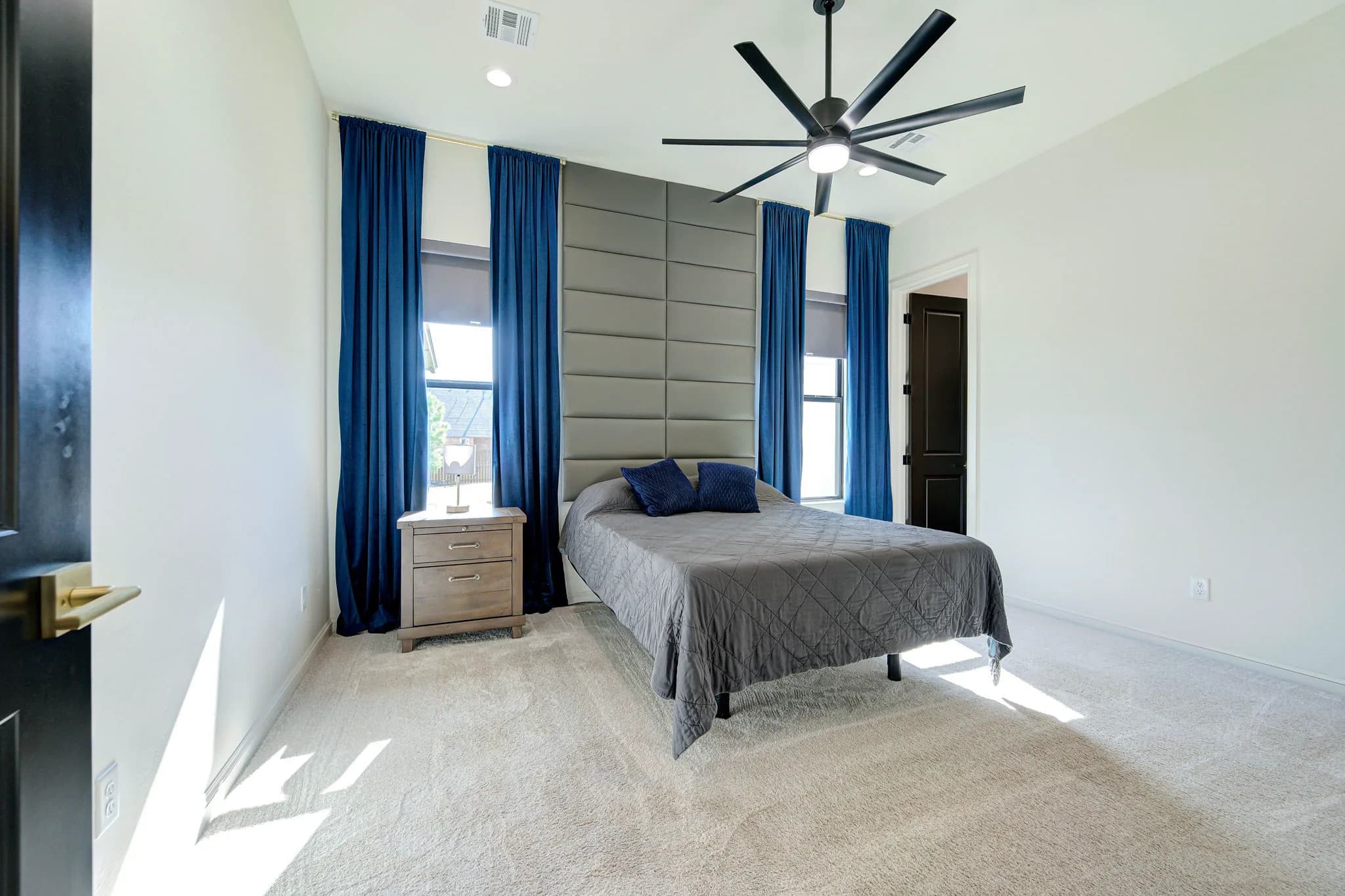 Secondary bedroom with an upholstered accent wall, floor-length drapes, carpet, and an oversized ceiling fan