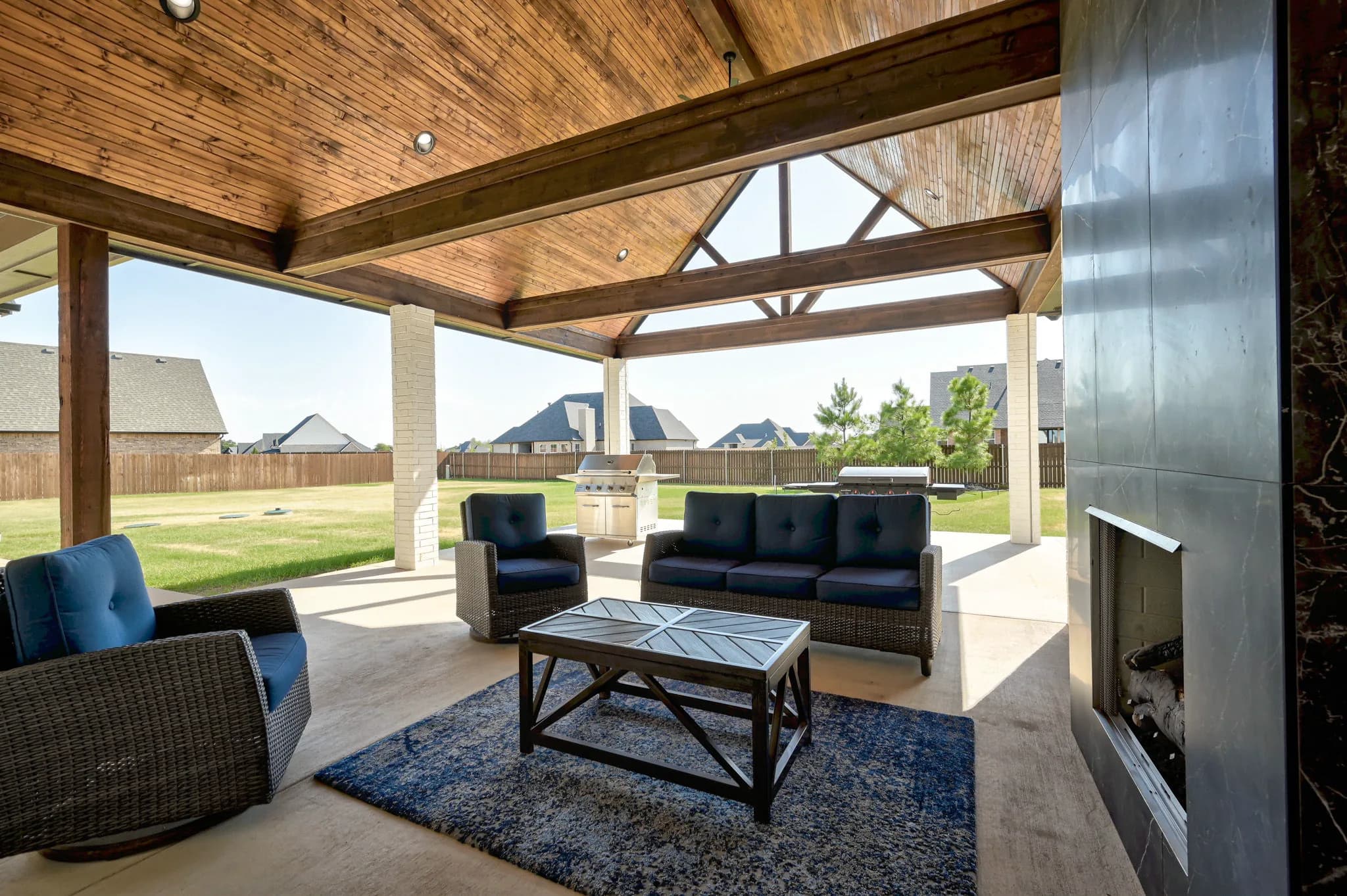 Covered back patio with a vaulted stained-wood ceiling, a floor-to-ceiling slate gas fireplace, and wicker seating overlooking the backyard