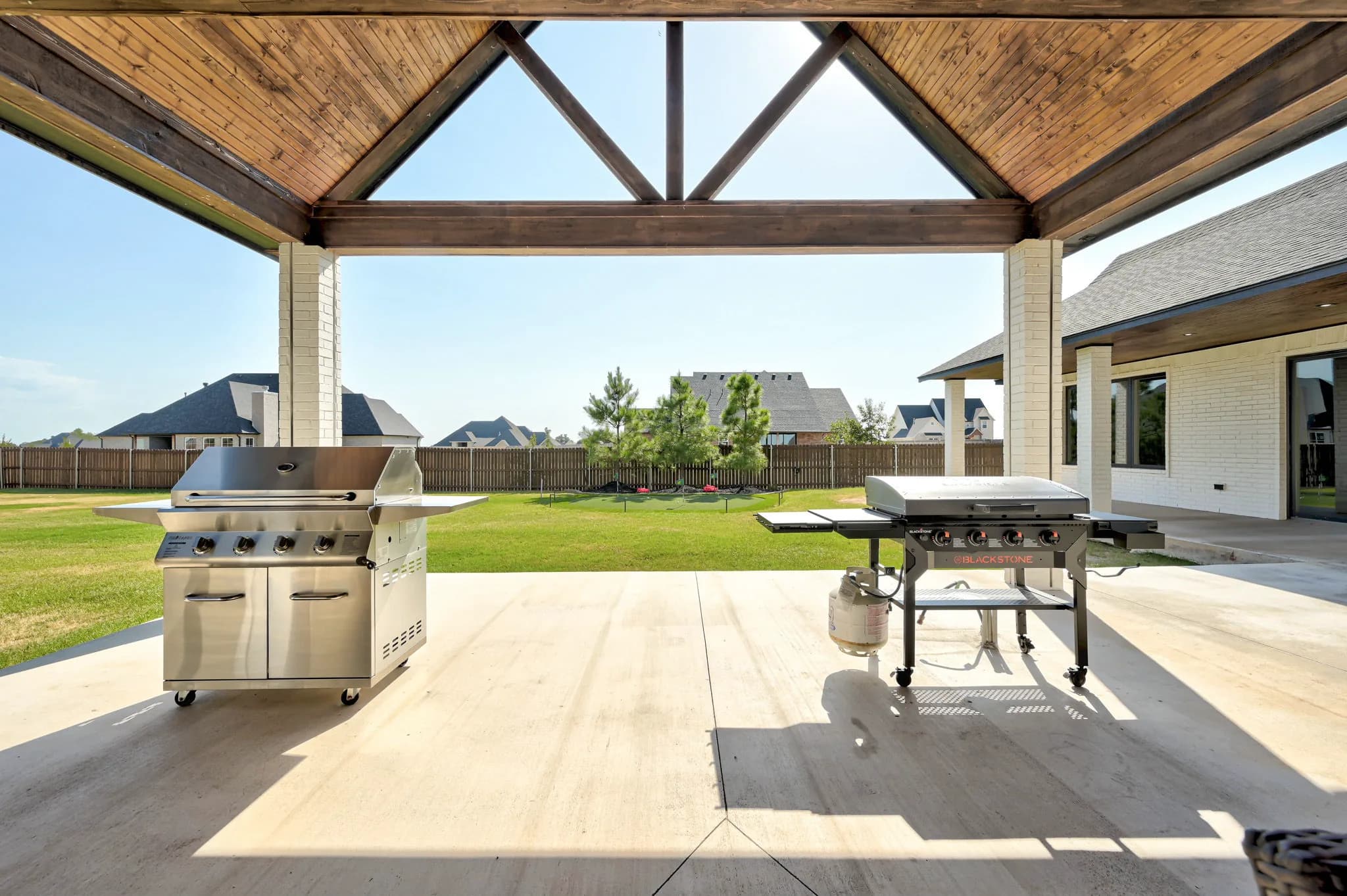 Covered patio grilling area with a gas grill and griddle, opening to the lawn and backyard putting green