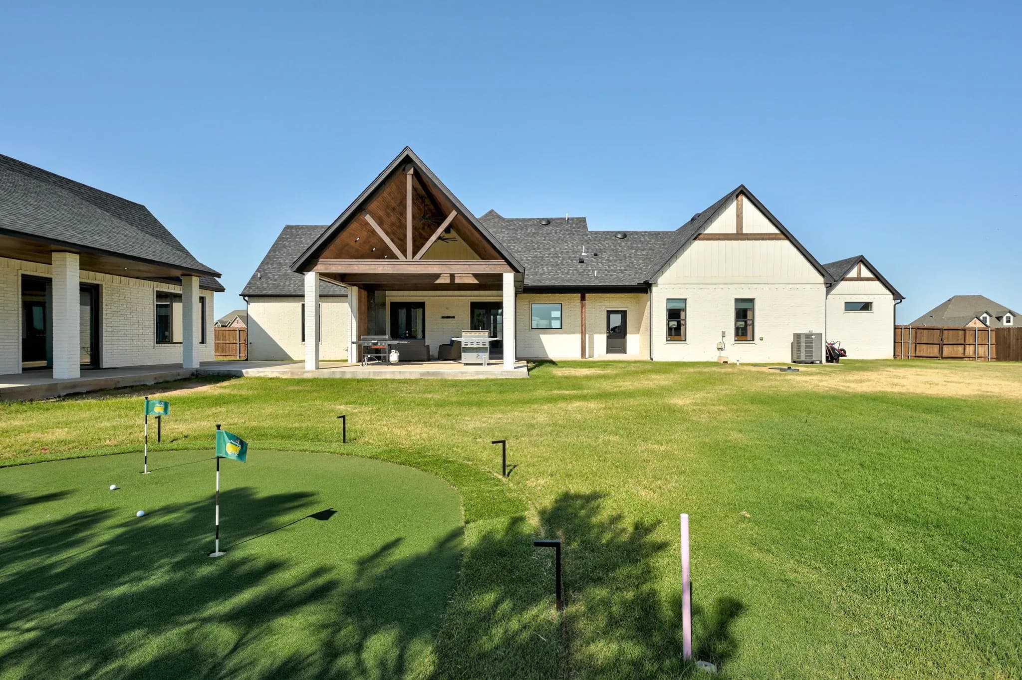 Rear exterior showing the vaulted covered patio centered between the main home and the detached building, with the putting green in the foreground
