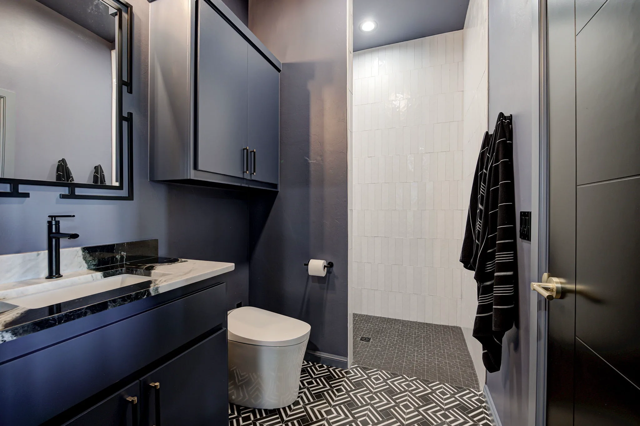 Full bath in the entertainment building with a tiled walk-in shower, patterned floor tile, and a marble-top vanity