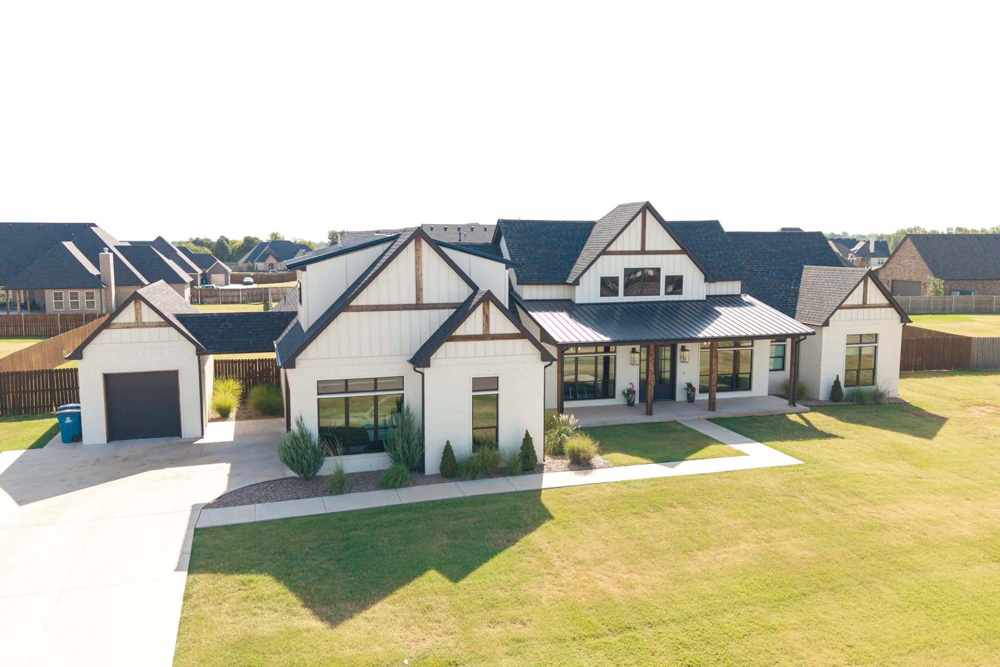 Aerial view of the front elevation showing the modern farmhouse, attached and detached garages, the driveway, and the landscaped lawn