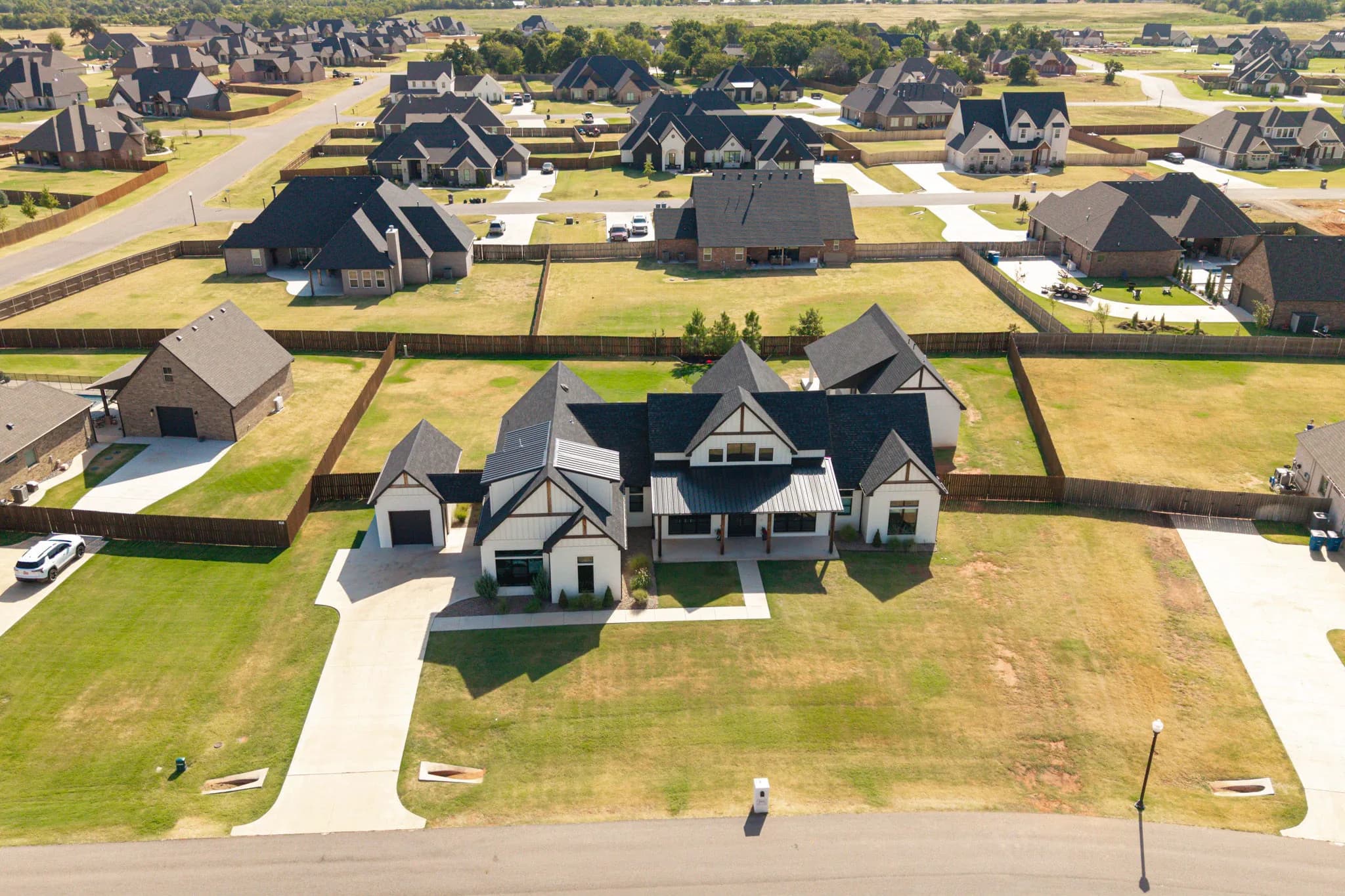 Aerial view of the full fenced lot showing the main home, the detached building, and the backyard putting green within the surrounding neighborhood