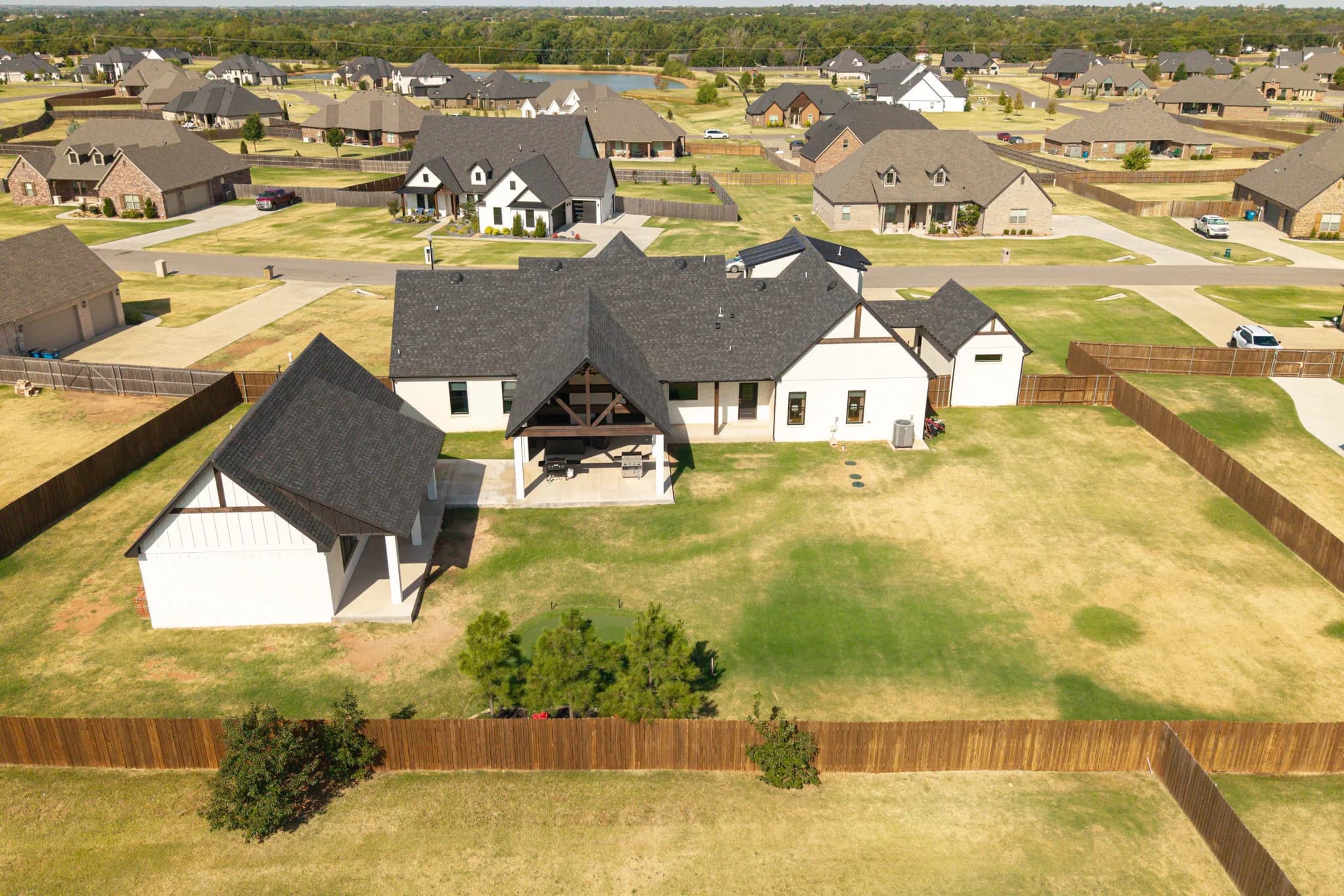 Aerial view of the rear of the property showing the covered patio, the backyard putting green, and the detached entertainment building on the fenced lot